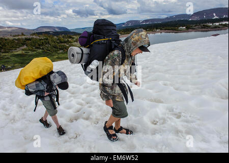 Jungen überqueren ein Schneefeld über fünf Punkt See während einer Rucksack-Reise durch die hohe Uintas Wilderness Area, Uintas Range, Utah Stockfoto