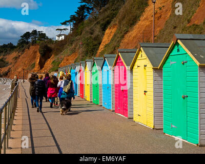 Urlauber, die entlang der Esplanade im Seaton Devon England UK mit bunten Strandhäuschen auf der einen Seite Stockfoto