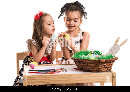 Zwei kleine Mädchen bemalen von Ostereiern und sitzen zusammen am Tisch isoliert auf weißem Hintergrund Stockfoto