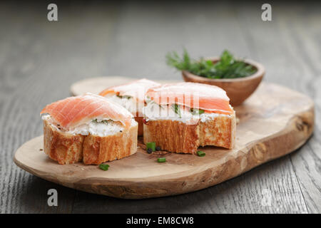 Baguette Scheiben mit geräuchertem Lachs und Käse-Sahne auf Holztisch Stockfoto