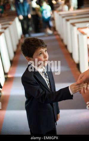 Sieben Jahre Alter spanischer Junge schüttelt die Hand des Priesters in der Kirche nach Erhalt der Sacrement der Erstkommunion.  Model-Release Stockfoto