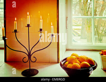 Stilleben, Korb mit Orangen in der Nähe eines Fensters und brennenden Kerzen auf Eisen Kerzenständer. Jahrgang Instagram-Effekt hinzugefügt. Stockfoto