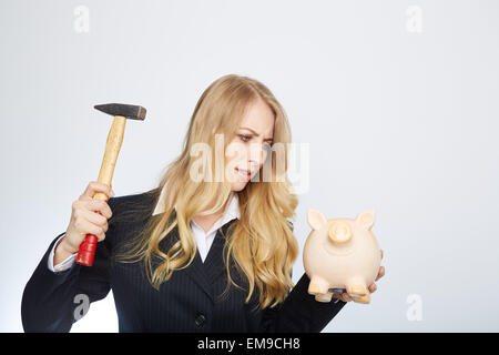 Ernsthafte Geschäftsfrau hält ein Sparschwein und hammer Stockfoto