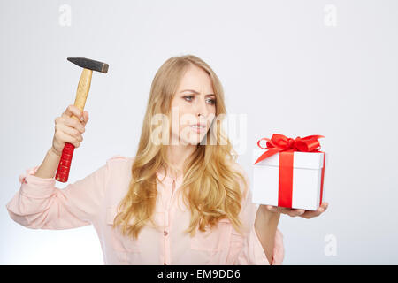 Junge, blonde Frau mit Geschenkbox und einem Hammer in der Hand. Stockfoto