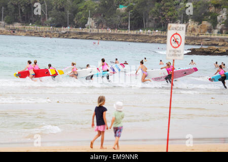 Schülerinnen und Schüler einer Surf-Schule läuft in die Wellen mit ihren Surfbrettern am Strand von Manly, Sydney, Australien. Stockfoto