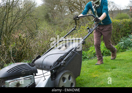 Eine ältere Frau, die den Garten mähen Gras mit einem Benzin Rasenmäher bei einer ländlichen Landschaft Eigenschaft auf einer trockenen Wolke Nachmittag im Frühjahr Carmarthenshire, West Wales UK Kathy deWitt Stockfoto