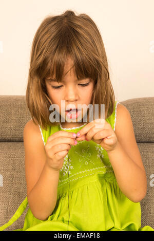 Kleine Mädchen machen eine Halskette aus einer Reihe von Kinderschmuck Stockfoto