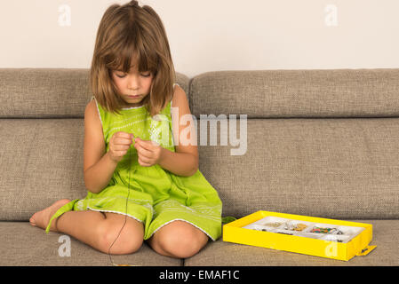 Kleine Mädchen machen eine Halskette aus einer Reihe von Kinderschmuck Stockfoto