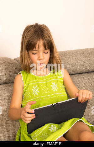 Kleine Mädchen spielen mit einem digitalen Tablet zu Hause auf dem sofa Stockfoto