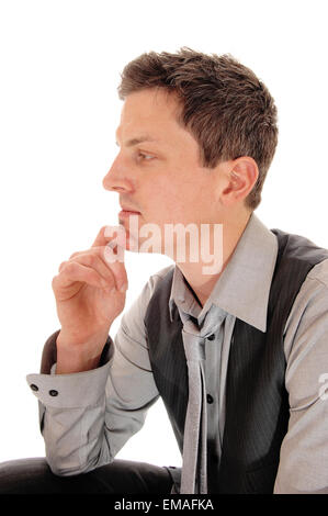 Ein junger Geschäftsmann sitzt isoliert für weißen Hintergrund mit einer Hand am Kinn in einem grauen Hemd, Weste und Krawatte. Stockfoto