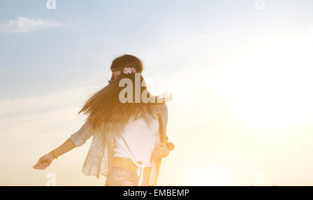 Eine junge Frau Skateboard in ihren Händen hält. Das Mädchen im freudigen Gefühle. Im Freien, Lifestyle. Voller Sonnenschein Bild. Stockfoto