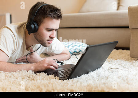 Mann auf dem Boden mit Kopfhörer auf laptop Stockfoto