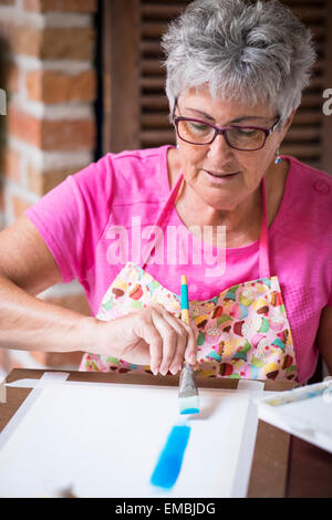 Eine reife Frau, die blaue Hintergrundfarbe auf ihre Malerei Bürsten. Stockfoto