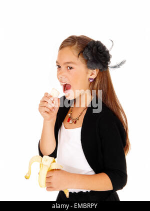 Ein acht Jahre altes Mädchen hielt eine Banane in der Hand zu essen, für weißen Hintergrund isoliert. Stockfoto