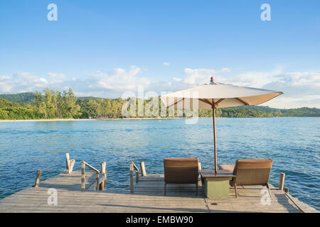 Sommer, Reisen, Urlaub und Ferien-Konzept - Liegestühle und Sonnenschirm am Schreibtisch aus Holz gegen blauen Himmel in Phuket, Thailand Stockfoto