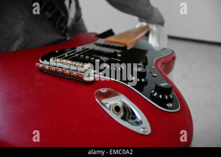 Unbekannter Mann reinigt seine e-Gitarrenhals mit einem weißen Tuch über dem Knie Stockfoto