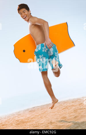 Ein junger Mann hält ein Surfbrett am Strand Stockfoto