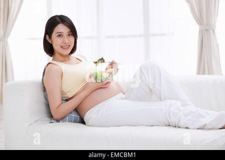 Schwangere Frauen essen Salat stützte sich auf dem sofa Stockfoto