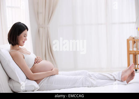 Die schwangere Frau auf dem Bett sitzen Stockfoto