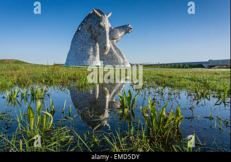 Das Kelpies Pferdeskulptur-Denkmal in Falkirk, Schottland, Großbritannien an einem sonnigen Tag vor blauem Himmel. Grünes Gras und Reflexion im Wasser. Stockfoto