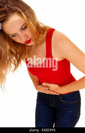 Eine junge, blonde Frau in einem roten T-shirt und Jeans stehen für weißen Hintergrund isoliert halten ihr Magen Schmerzen. Stockfoto