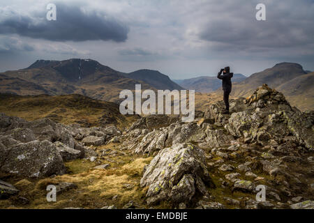 Frau, die im Frühling, Lake District, Großbritannien, durch Ferngläser den Blick von Glaramara aus betrachtet, mit Großem Ende im Hintergrund Stockfoto