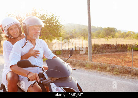 Älteres Paar Reiten Motorroller auf Landstraße Stockfoto