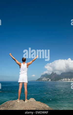 Sportler im weißen Sport einheitliche stehen mit Champion vor Rio De Janeiro Brasilien Skyline bei Arpoador Ipanema erhobenen Armen Stockfoto