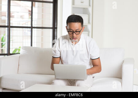 Southeast Asian männlich über Internet zu Hause auf Sofa schockiert Stockfoto