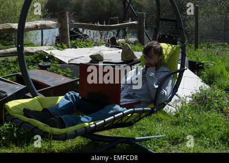 Junger Mann, ist entspannend, draußen im Garten. Überarbeitung zu tun und Gaming, ein Videospiel draußen spielen. Stockfoto