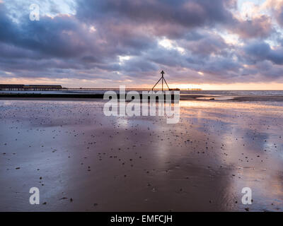 Ein wunderbarer Sonnenaufgang am Strand bei Ebbe geben erstaunliche farbige Reflexionen über die glitzernden Strand mit Aussicht zu den piers Stockfoto
