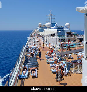Blick auf das geschäftige Sonnenbaden und das Schwimmbaddeck auf einem Kreuzfahrtschiff Ozeanliner während eines Sonnentages mit blauem Himmel auf dem Meer, das durch das Mittelmeer fährt Stockfoto
