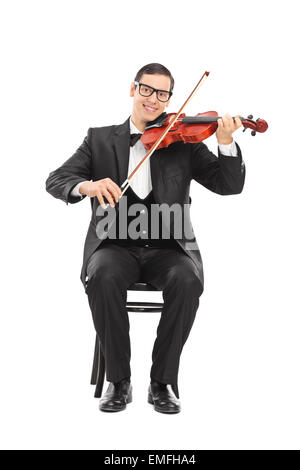 Fröhliche junge Geigerin spielen eines akustischen Violine sitzend auf einem Holzstuhl isoliert auf weißem Hintergrund Stockfoto