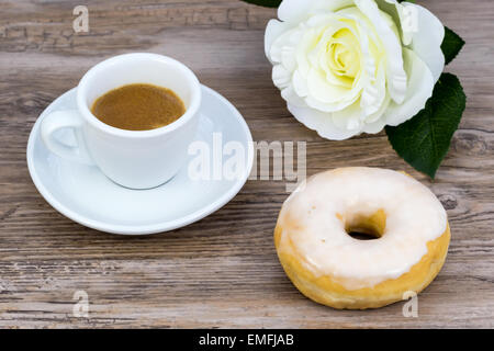 Espresso mit einem glasierten Donut und eine weiße Rose in unscharfen Hintergrund auf einem Holztisch von oben Stockfoto