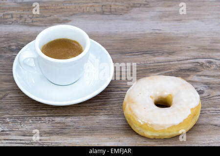 Espresso mit einem glasierten Donut auf einem Holztisch verwischt leicht Hintergrund von oben Stockfoto