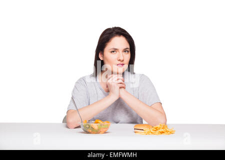 Bild der Frau mit Obst und Hamburger denken vor Wahl auf weißem Hintergrund, gesunde gegen Junk-Food Konzept Stockfoto