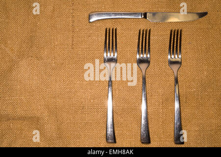 Drei Gabeln und Messer auf eine alte Tischdecke Stockfoto