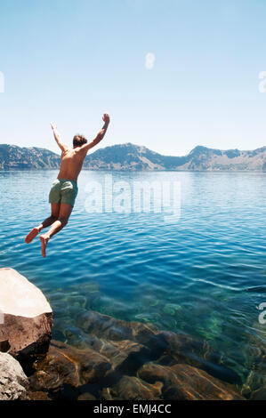 Junger Mann in See springen Stockfoto