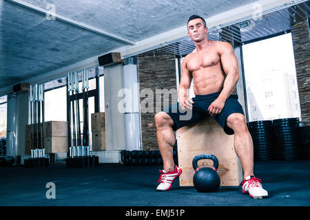 Muskulös, gut aussehender Mann auf Fit Box im Fitness-Studio sitzt und Blick in die Kamera Stockfoto