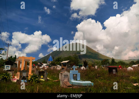 Ein ländlicher Friedhof im Hintergrund des Mount Lokon, einem aktiven Vulkan in Tomohon, Nord-Sulawesi, Indonesien. Stockfoto