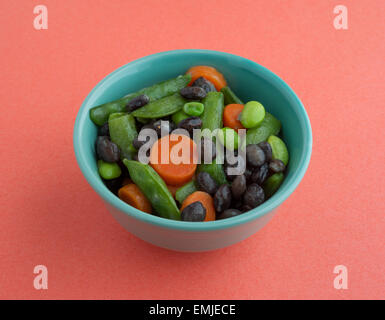 Verschiedene gekochte Buttergemüse in einer kleinen Schüssel auf einem orangefarbenen Hintergrund durch natürliches Licht beleuchtet. Stockfoto