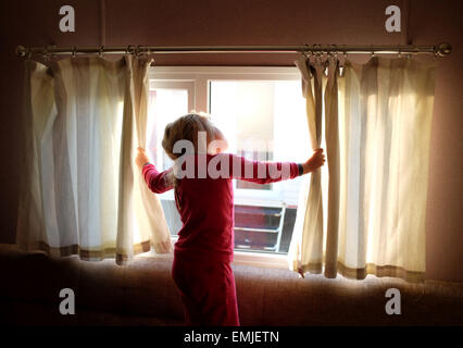 Ein verschlafenes junges Mädchen im Schlafanzug öffnet die Vorhänge, Blick aus dem Fenster zu Beginn eines neuen Tages