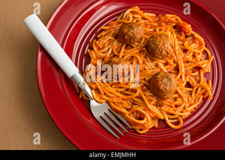 Draufsicht eines Spaghetti und Fleischbällchen TV-Dinner auf einem roten Teller mit einer Gabel auf einem Tan Tischdecke. Stockfoto