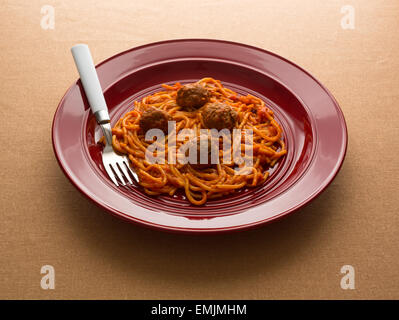 Ein Spaghetti und Fleischbällchen TV Dinner auf einem roten Teller mit einer Gabel auf einem Tan Tischdecke von Fensterlicht beleuchtet. Stockfoto