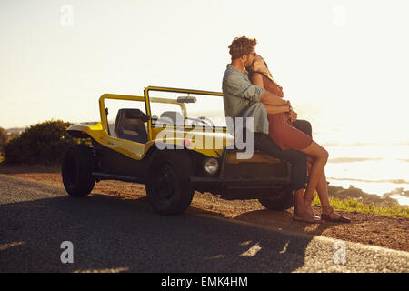 Romantische junges Paar auf Motorhaube ihres Autos sitzen und küssen. Junges Paar teilen einen leidenschaftlichen Kuss auf Reise. Stockfoto