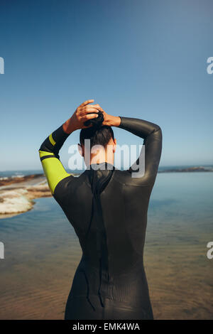 Heckansicht des jungen Triathleten auf dem See, die Vorbereitung auf ein Rennen einen Neoprenanzug tragen. Weiblichen Triathlon-Sportler binden ihr Haar und ge Stockfoto