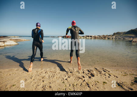 Rückansicht der Teilnehmer trugen Anzüge laufen ins Wasser für einen Triathlon-Rennen. Triathleten üben. Stockfoto