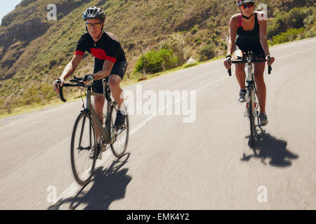 Zwei Athleten bergab auf Rennrädern. Mann und Frau Radfahrer fahren auf der Landstraße. Triathlon-Training. Stockfoto