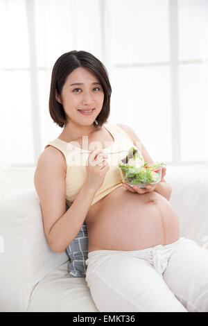 Schwangere Frauen essen Salat stützte sich auf dem sofa Stockfoto