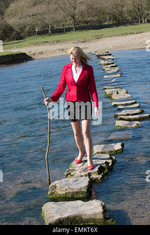 Stepping Stones elegant gekleidete Frau Kreuzung Fluß mit einem Ast für Gleichgewicht. Fuß über den Fluss Ogmore im Süden W Stockfoto